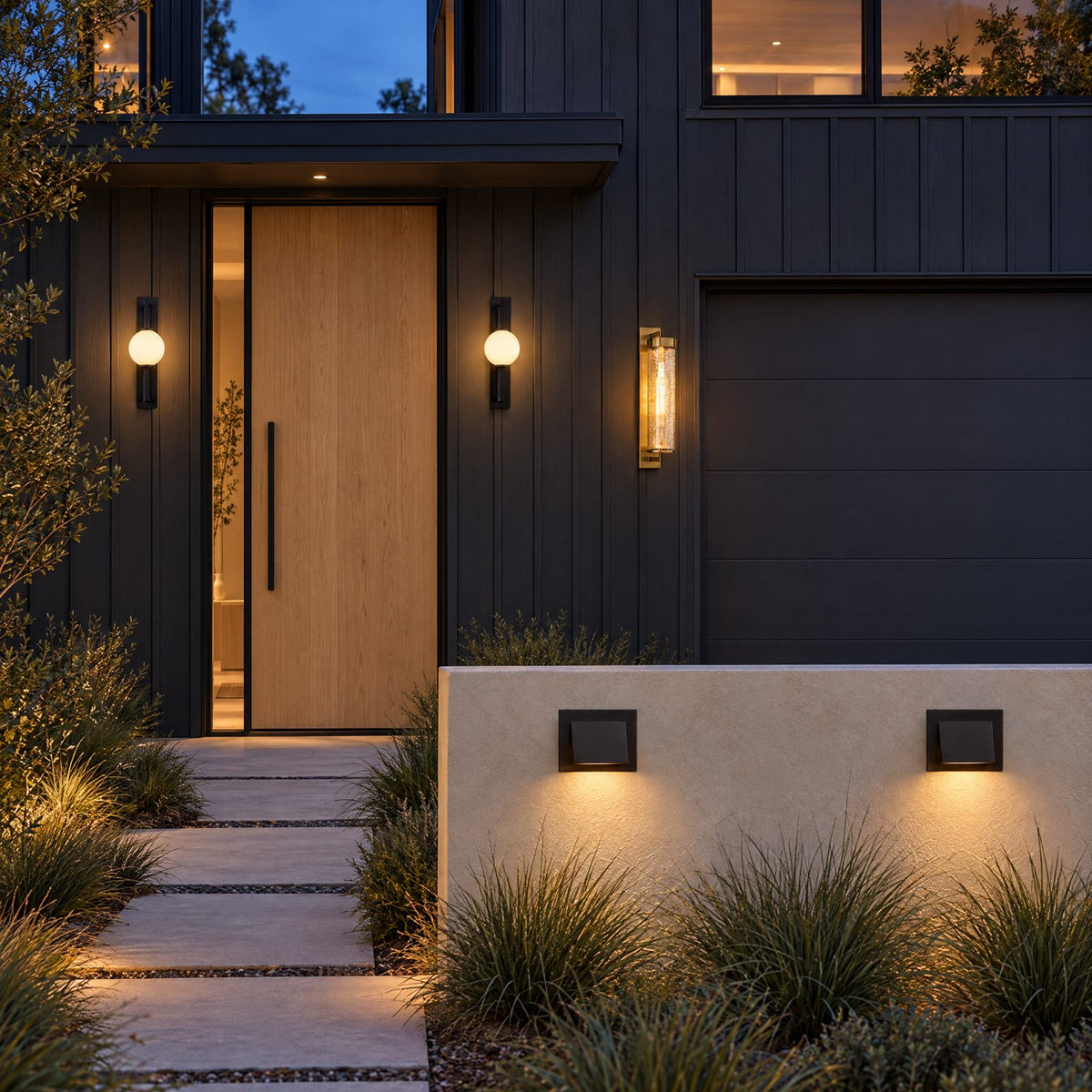 Shop the look: Modern house at dusk with Troy Darwin black lantern sconces flanking the front door, Kelly Wearstler Liaison brass sconces at the garage and Kelly Wearstler Esker bronze sconces along a garden wall